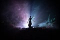 Silhouette Of Blurred Giant Lady Justice Statue With Sword And Scale Standing Behind Crowd At Night With Foggy Fire Background.