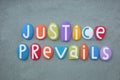 Justice Prevails, creative slogan composed with multi colored stone letters over green sand