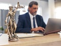 Justice, statue and man in office with laptop at law firm desk, online research for court advice and senior lawyer