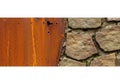 Juxtaposition of rustic rusty metal panel against textured stone wall surface Royalty Free Stock Photo