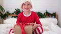 Little boy shakes gift box to find out what is inside. Child in Christmas Santa hat and pajama. Fulfilling children