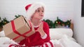 Little boy shakes gift box to find out what is inside. Child in Christmas Santa hat and pajama. Fulfilling children
