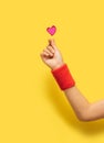 K pop concept. A girl hand with red sport cotton sweat bands showing fingers heart gesture. Red glitter heart above. Optimistic