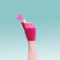 K pop concept. A girl teenager hand with magenta glove showing finger heart gesture. Red heart above. Unique blue background
