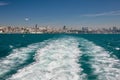 Seagulls fly over the sea behind the boat. Ships wake. The ship is leaving the big city.