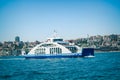 Wide angle view of blue white ferryboat carrying cars and vehicles moving on Marmara Sea and city appears behind in a clear air