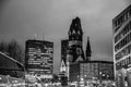 Black and white photo of night cityscape of Breitscheidplatz square with skyscrapers and clock tower of cathedral