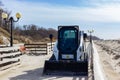 Kaliningrad, Russia - March 31, 2019: Red skid loader at wooden footpath of Baltic sea on sunny spring day