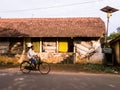 An Indian man rides a bicycle past a rustic building with slanted roofs in a