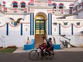 Boys riding a bicycle past a grand colorful mansion with white walls in