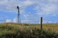 Kansas colorful landscape with a Windmill, blue sky, fence, and yuccas out in the country.