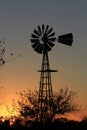 Kansas Sunset with a Windmill and tree silhouette that`s bright and colorful with the Sun and a fence. Royalty Free Stock Photo