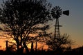 Kansas Sunset with a Windmill and tree silhouette that`s bright and colorful with the Sun and a fence. Royalty Free Stock Photo