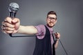 Karaoke man sings the song to microphone, singer with beard on grey background. Funny man in glasses holding a microphone