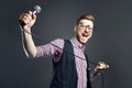 Karaoke man sings the song to microphone, singer with beard on grey background. Funny man in glasses holding a microphone