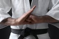 Karate coach wearing kimono and black belt on dark background, closeup