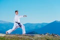 Karate man in a kimono performs a front hand kick Choku-zuki while standing on the green grass on top of a mountain Royalty Free Stock Photo