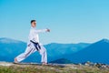 Karate man in a kimono performs a front hand kick Choku-zuki while standing on the green grass on top of a mountain Royalty Free Stock Photo