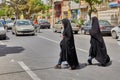 Two Muslim women cross roadway of city street, Kashan, Iran.