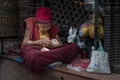 A 100-year-old Tibetan Buddhist nun sitting next to a prayer wheel at the entrance to the Boudhanath stupa, Kathmandu Royalty Free Stock Photo