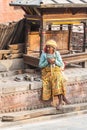 Kathmandu / Nepal - February 2016: Old poor barefoot woman in bright traditional clothes sitting on the sun on Kathmandu street