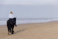 Girl with blue vest rides a black horse on the beach Royalty Free Stock Photo