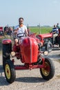 Man with sunglasses and white Tshirt on red tractor gives a thumbs-up as he starts driving.