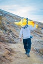 KAWEH IJEN, INDONESIA: Local miner carrying heavy load of yellow sulfur rocks up mountain side, tourist hiking