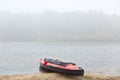 Kayak on river bank in foggy early morning, black and red canoe on sand shoe, fog above water, rowing boat Royalty Free Stock Photo