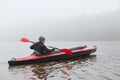 Kayaker paddling in water, holding oar in hands, sportsman in canoe, water sport, guy in jacket rowing boat in cold autumn foggy