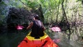 Kayaker rows with paddle close to cliff and tree branches
