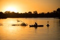 Kayaker silhouette at sunset on a river with floating logs and branches. Outdoor water sports