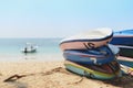 Kayaks stacked on sand beach in front of boat in the sea.