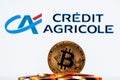 Golden bitcoin in a pile of coins on the background of Credit Agricole bank logo