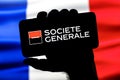 Smartphone with Societe Generale bank logo in clenched hand on background of France flag Royalty Free Stock Photo