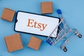 Smartphone with Etsy logo on the screen, shopping cart and parcels Royalty Free Stock Photo
