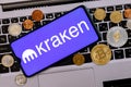 A smartphone with the Kraken logo metal coins, bitcoin, ethereum on a laptop keyboard