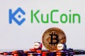 Golden bitcoin with two buy-sell cubes in a pile of coins on the background of the KuCoin logo. The concept of buy-sell choice Royalty Free Stock Photo