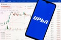 A smartphone with the Upbit logo on the background of the live trading webpage. Upbit dashboard