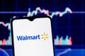 Walmart is an American multinational retail corporation. Smartphone with Walmart logo on the background of the stock chart