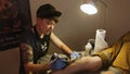 Concentrated Girl Tattooist Draws Picture on Guy Leg