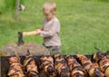 Kebabs grilling on a BBQ as a small boy chops wood