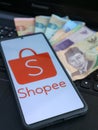 Kebumen, Indonesia - November 7, 2024 : Smartphone showing Shopee logo with Indonesian Rupiah banknotes and laptop keyboard