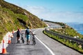 Keem road, Ireland - 05.28.2021: Couple tourists walking with bicycles on a small mountain road. Travel and outdoor activity. Man