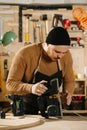 Keen carpenter in a watch cap in a big workshop. Checking electric plane Royalty Free Stock Photo