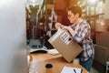 Keen female warehouse worker closing box with cello tape, making a mess