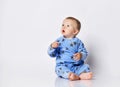 Cute barefooted blond baby boy toddler in blue fleece jumpsuit with stars sits on the floor looking up with opened mouth