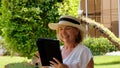 keen Senior female blonde businesswoman in hat uses tablet pc, digital tablet for business work or study in her own