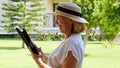 keen Senior female blonde businesswoman in hat uses tablet pc, digital tablet for business work or study in her own
