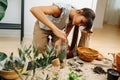 Keen woman in living room planting inside glass bottle, using stick Royalty Free Stock Photo